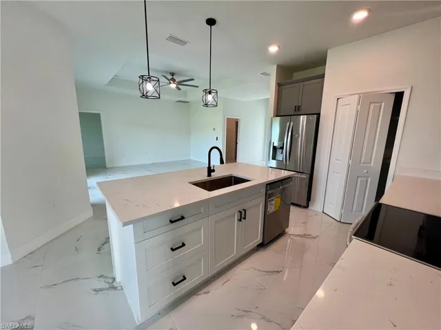 Kitchen with appliances with stainless steel finishes, hanging light fixtures, light stone counters, ceiling fan, and sink