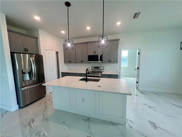 Kitchen with appliances with stainless steel finishes, hanging light fixtures, light QUARTZ counters, a center island with sink, and sink
