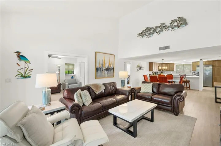 Living room with a towering ceiling, a notable chandelier, light wood-style floors, and visible vents