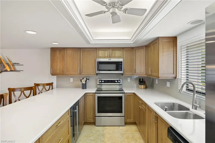 Kitchen with a sink, light countertops, decorative backsplash, a tray ceiling, and appliances with stainless steel finishes