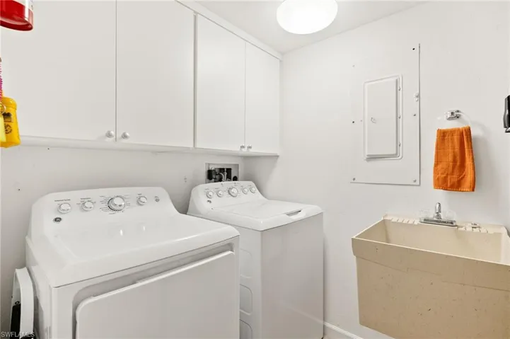 Washroom with a sink, washer and clothes dryer, cabinet space, and electric panel