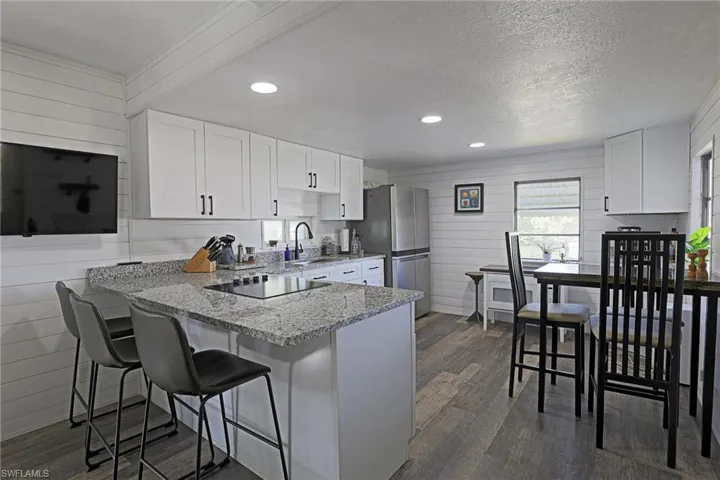 Kitchen featuring white cabinets, light stone counters, a peninsula, recessed lighting, and wood walls
