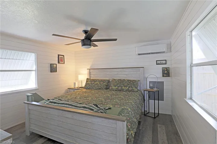 Bedroom with wood walls, ceiling fan, dark wood-style flooring, a wall unit AC, and a textured ceiling