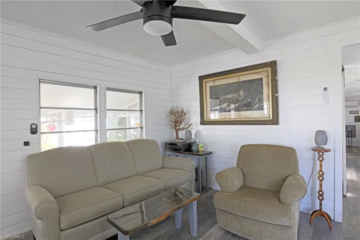 Living room featuring beamed ceiling, wood finished floors, wood walls, and a ceiling fan