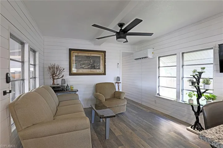 Living area featuring wood walls, dark wood-style flooring, healthy amount of natural light, ceiling fan, and a wall unit AC