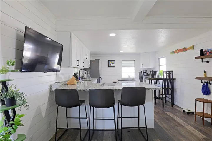 Kitchen featuring white cabinets, wood walls, light stone counters, a breakfast bar, and a peninsula