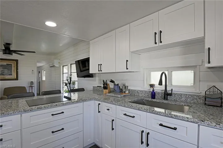 Kitchen featuring white cabinetry, light stone counters, open floor plan, wood walls, and recessed lighting
