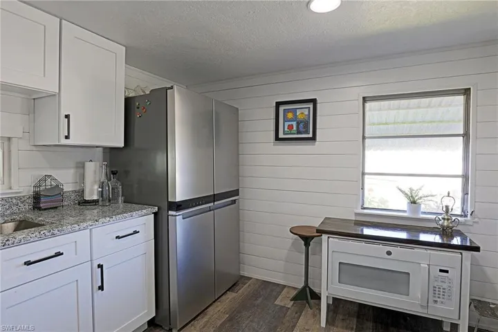 Kitchen featuring white microwave, white cabinetry, dark wood-style floors, a textured ceiling, and light stone countertops