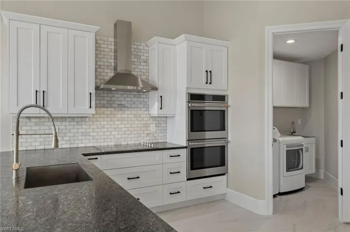 Kitchen featuring white cabinets, sink, wall chimney exhaust hood, double oven, and washing machine and dryer