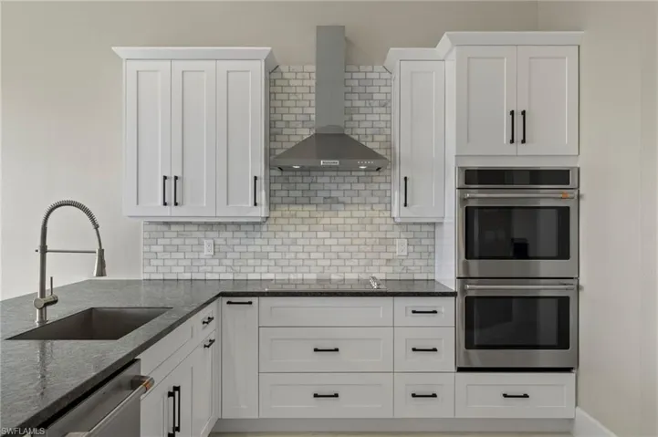 Kitchen featuring white cabinets, appliances with stainless steel finishes, sink, wall chimney exhaust hood, and dark stone counters