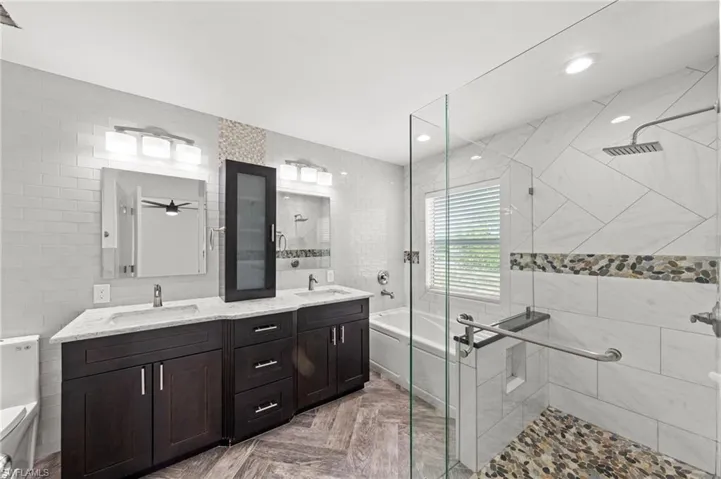 Modern bathroom featuring a double vanity with dark wood cabinetry and light countertops, a glass-enclosed shower with pebble flooring, and a separate bathtub