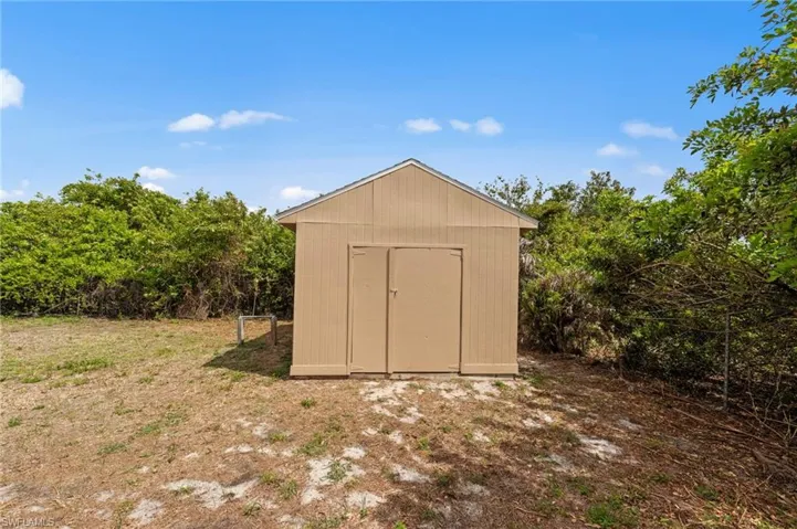 The property features a neutral-toned shed with a gabled roof, set on a patch of dry grass