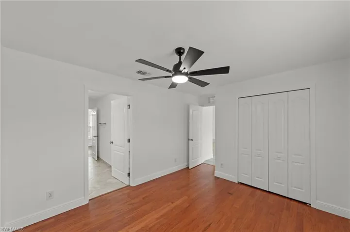 This room features hardwood floors, white walls, a black ceiling fan with a light fixture, and white bi-fold closet doors