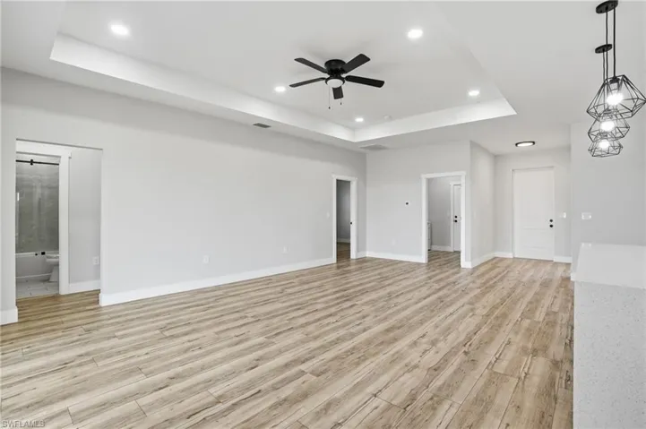 Unfurnished living room featuring a raised ceiling, light wood-type flooring, a ceiling fan, and recessed lighting