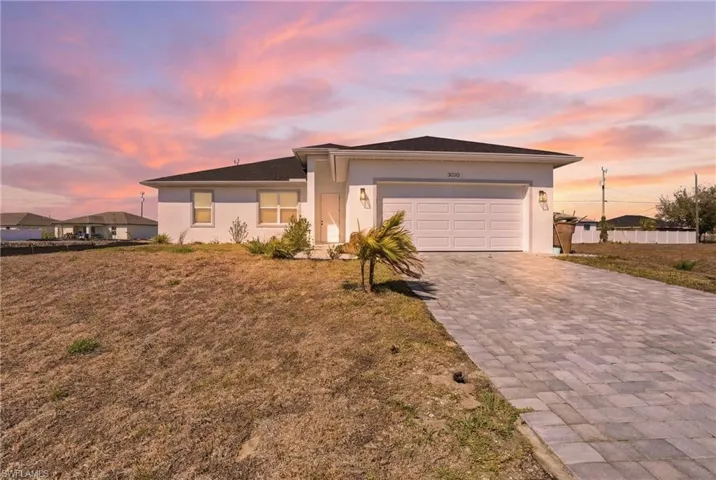 View of front of home featuring stucco siding, decorative driveway, an attached garage, and a front lawn