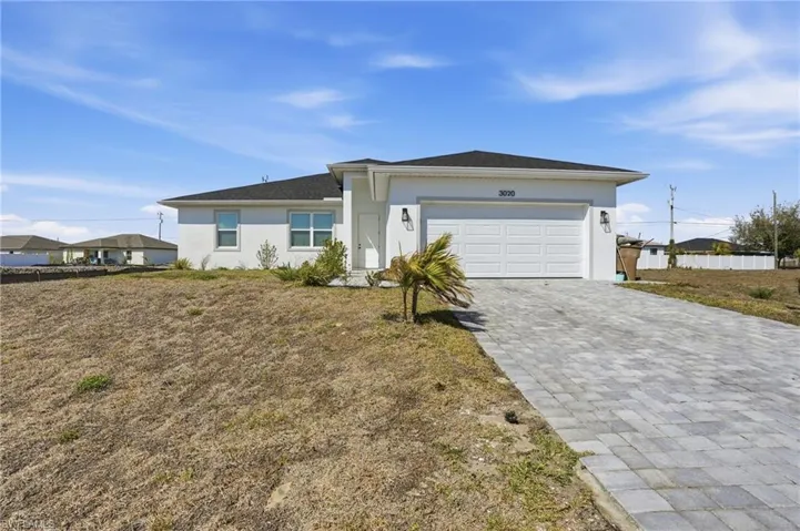Single story home with decorative driveway, stucco siding, a garage, and a front lawn