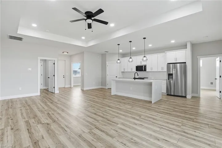 Kitchen with white cabinetry, stainless steel appliances, a ceiling fan, open floor plan, and a kitchen island with sink
