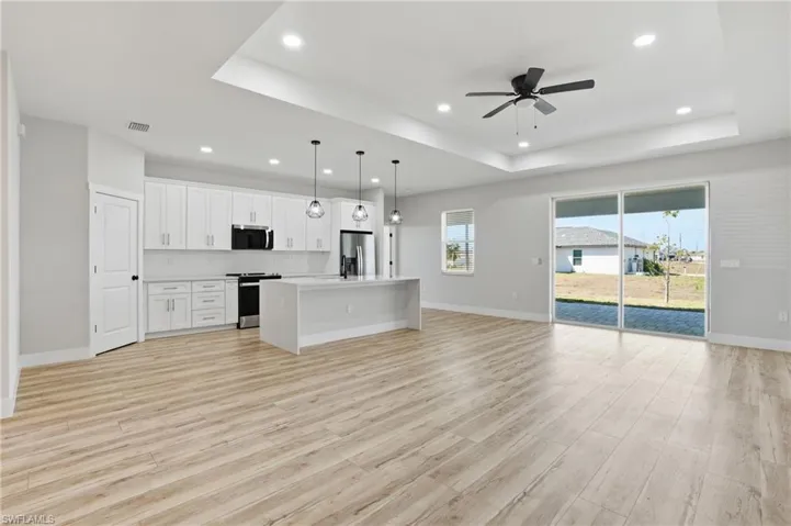 Kitchen with open floor plan, a kitchen island with sink, decorative light fixtures, white cabinetry, and stainless steel appliances