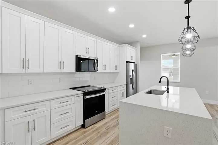 Kitchen featuring stainless steel appliances, white cabinets, light wood-type flooring, light stone counters, and decorative light fixtures
