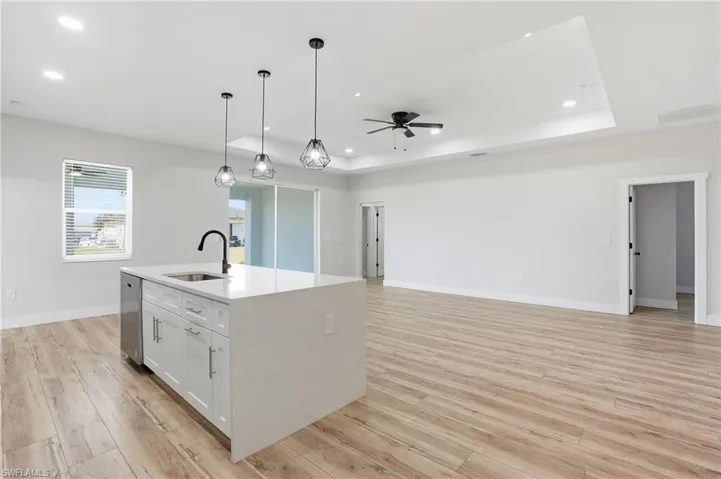 Kitchen with an island with sink, white cabinetry, light stone countertops, open floor plan, and light wood finished floors