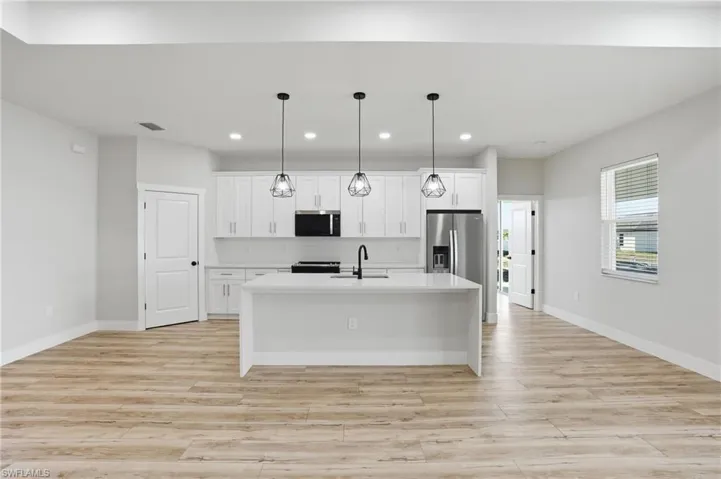 Kitchen featuring white cabinets, an island with sink, decorative light fixtures, light wood-style floors, and stainless steel appliances