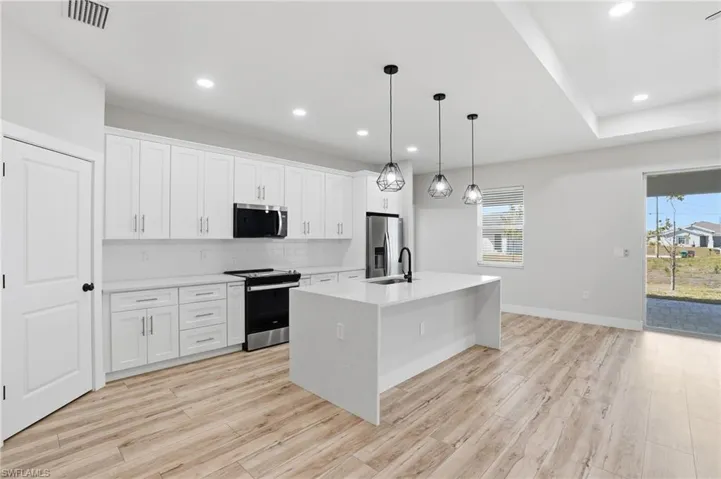 Kitchen featuring stainless steel appliances, an island with sink, white cabinets, decorative light fixtures, and decorative backsplash