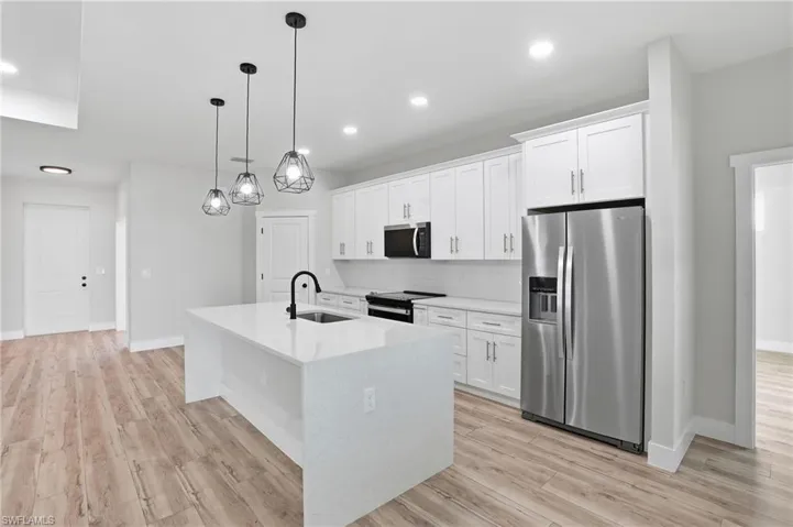 Kitchen with stainless steel appliances, white cabinets, light stone counters, light wood-style flooring, and a kitchen island with sink