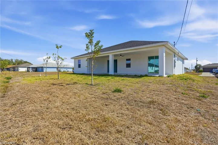 Rear view of property with stucco siding, a lawn, a patio, a ceiling fan, and roof with shingles