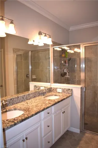 Full bathroom featuring a stall shower, double vanity, and crown molding