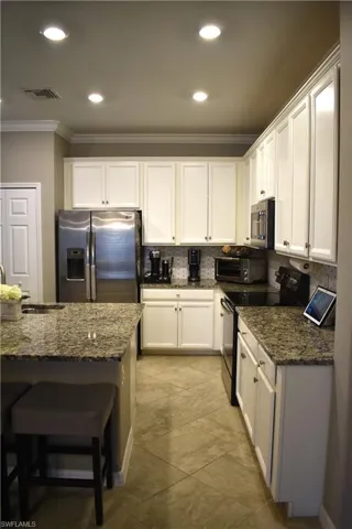 Kitchen featuring crown molding, stainless steel appliances, dark stone countertops, white cabinetry, and recessed lighting