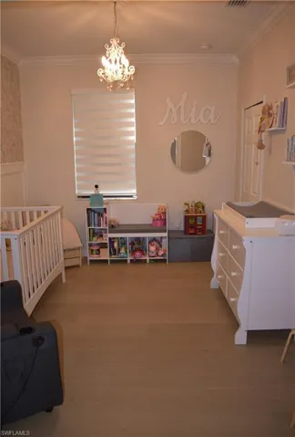 Bedroom with ornamental molding, hanging lights, light wood finished floors, and wainscoting