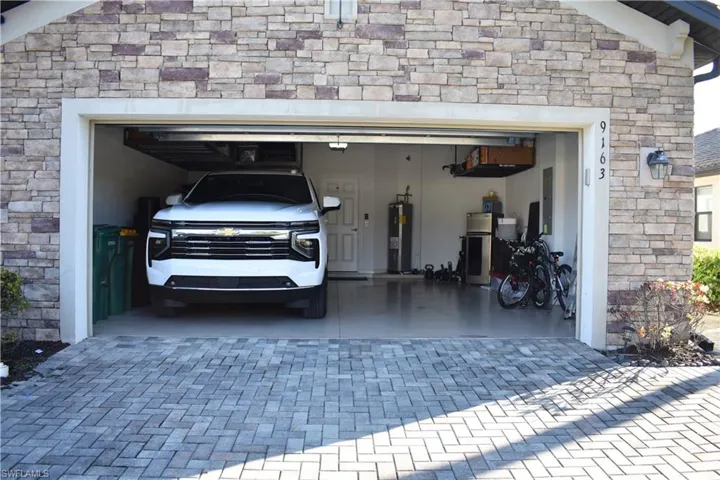Garage with decorative driveway, water heater, freestanding refrigerator, and electric panel