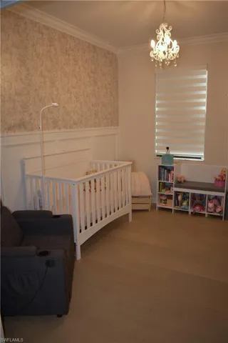 Bedroom featuring a wainscoted wall, crown molding, hanging lights, a decorative wall, and wood finished floors