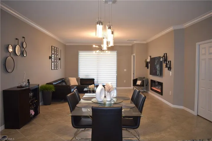 Tiled dining area with a chandelier, a glass covered fireplace, and ornamental molding