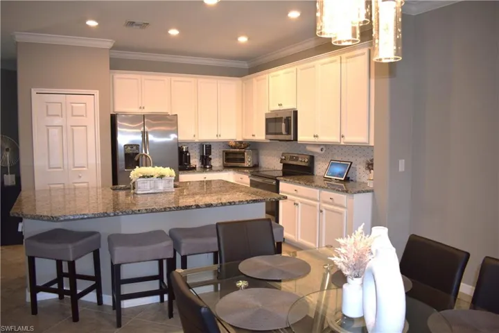 Kitchen featuring dark stone counters, stainless steel appliances, backsplash, crown molding, and an island with sink