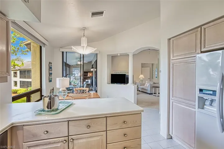 Kitchen with white refrigerator with ice dispenser, decorative columns, light countertops, lofted ceiling, and light tile patterned floors