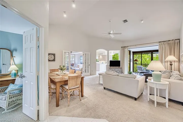 Living area featuring light carpet, healthy amount of natural light, ceiling fan, arched walkways, and high vaulted ceiling