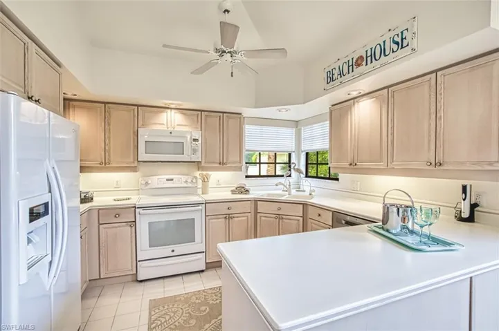 Kitchen featuring white appliances, a peninsula, light brown cabinets, light countertops, and a ceiling fan