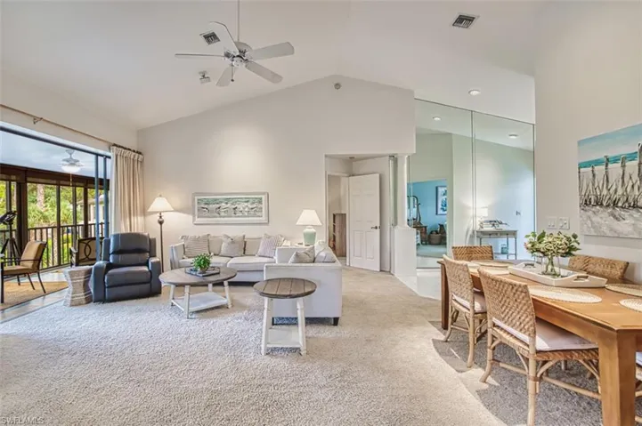 Living area with ceiling fan, high vaulted ceiling, and light colored carpet