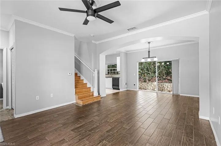 Spacious open-concept living area featuring wood-look tile flooring, light gray wall tones, and crown molding
