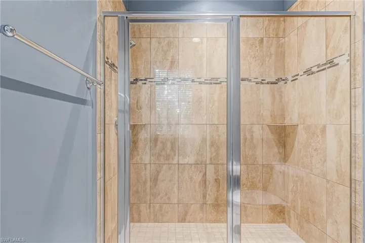 Walk-in shower featuring glass enclosure with brushed nickel framing, large format tan tile, decorative mosaic tile accent band, integrated corner shelf, and built-in bench