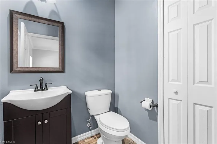 Powder room featuring a dark wood-finish vanity with a white ceramic sink, oil-rubbed bronze faucet, framed mirror, and wood-look flooring