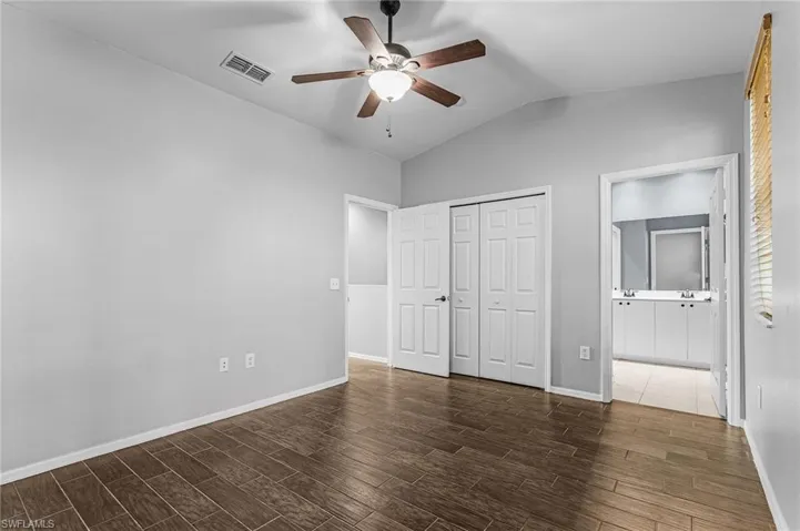 Spacious room featuring vaulted ceilings, wood-finish flooring, a ceiling fan with integrated lighting, and bi-fold closet doors