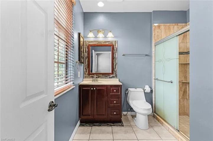Bathroom featuring a rich wood-finish vanity with a light-toned countertop, a frameless glass-enclosed shower with tile surround, and light tile flooring