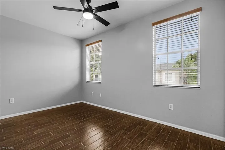Spacious room featuring wood-finish flooring, light grey walls, and a ceiling fan with integrated lighting