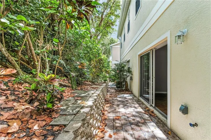 Backyard patio featuring a stone block retaining wall, paver pathway, sliding glass door access, and exterior wall sconce