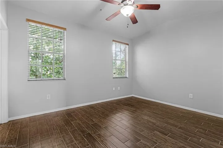 Neutral-toned interior with wood-finish tile flooring, two windows with blinds, and a ceiling fan with integrated lighting