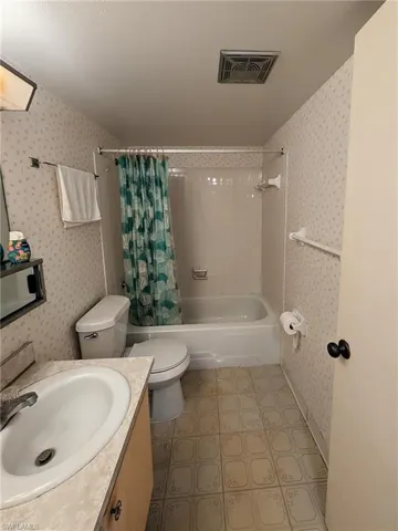 Full bathroom with vanity, wallpapered walls, shower / bath combo, and light floors
