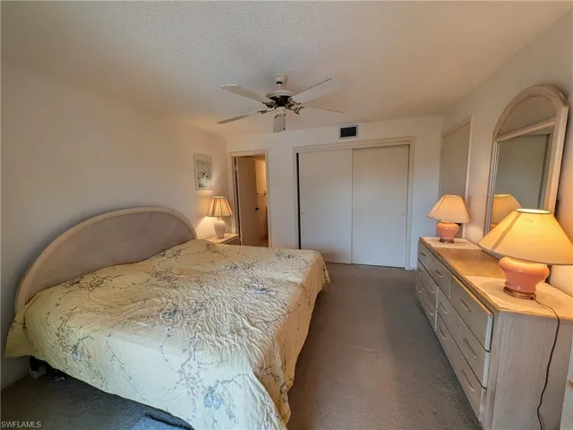 Bedroom with dark colored carpet, a textured ceiling, a closet, and a ceiling fan