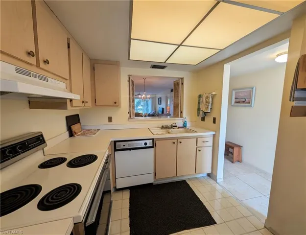 Kitchen with white appliances, a chandelier, light brown cabinetry, light countertops, and under cabinet range hood